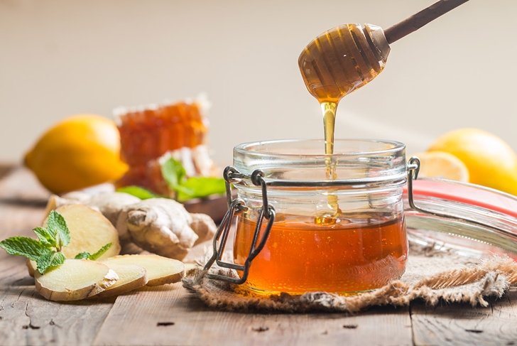 Honey in jar with honey dipper, ginger and lemon on wooden background