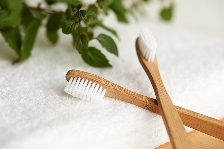 Close up of two bamboo toothbrushes on white towel with plant on background