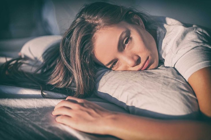 Tired woman lying in bed can\'t sleep late at night with insomnia. Asian girl with funny face sick or sad depressed sleeping at home.