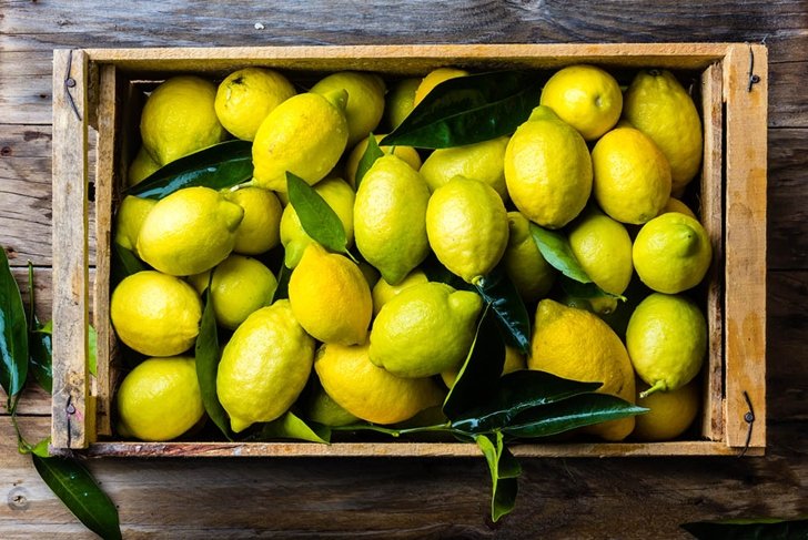 Fresh lemon with leaves. Lemon tree. Box of yellow lemons with fresh lemon tree leaves on wooden background. Top view